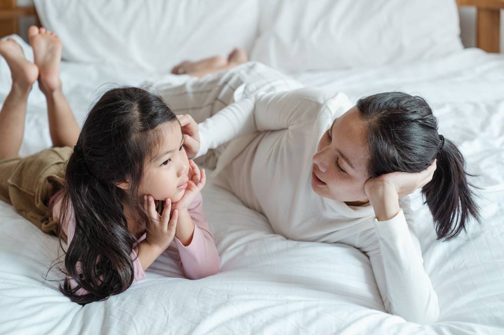 A mother lovingly talking to her daughter while lying on a bed